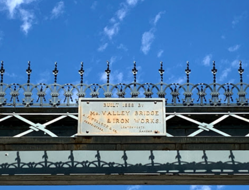Sign on a bridge reads "Built 1888 by McValley Bridge & Iron Works" against a blue sky with clouds.