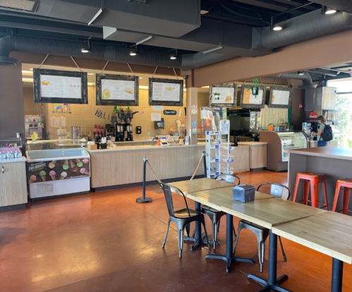 A modern café interior with a service counter, menu boards, and seating area featuring wooden tables and metal chairs.