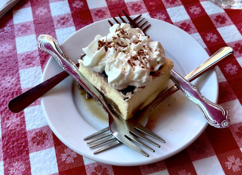 A slice of dessert topped with whipped cream and chocolate shavings, served on a plate with multiple forks.