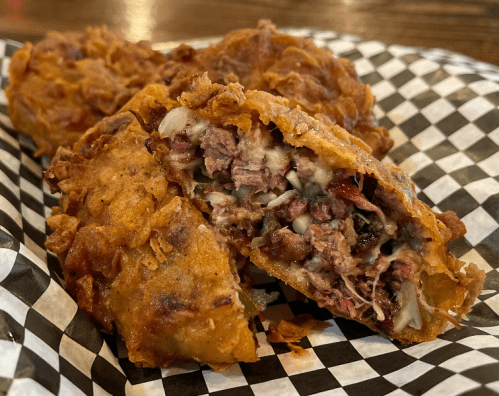 Crispy fried rolls filled with meat and cheese, served on a checkered paper plate.