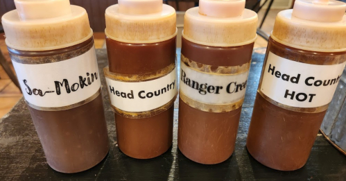 Four condiment bottles labeled "So-Mokin," "Head Country," "Ranger Creek," and "Head Country HOT" on a table.