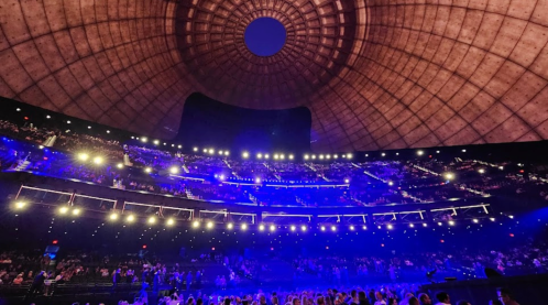 A concert venue with a large, dome-shaped ceiling and vibrant blue lights illuminating the audience below.