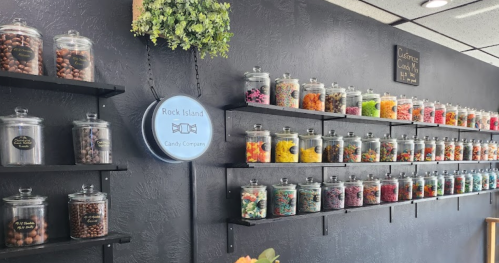 A colorful display of candy jars on shelves at Rock Island Candy Company, with a sign and greenery on the wall.