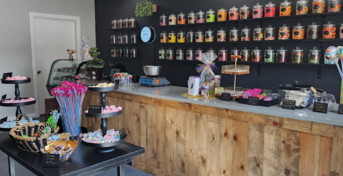 A colorful candy shop interior with jars of sweets on shelves, a display counter, and various treats on tables.