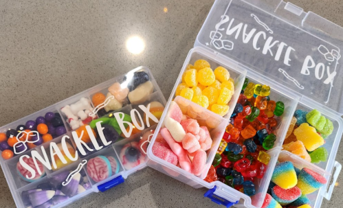 Two clear snack boxes filled with colorful candies, including gummies, jelly beans, and assorted sweets.