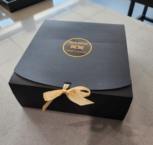 A black gift box with a yellow ribbon and a circular logo for Rock Island Candy Company on the top.