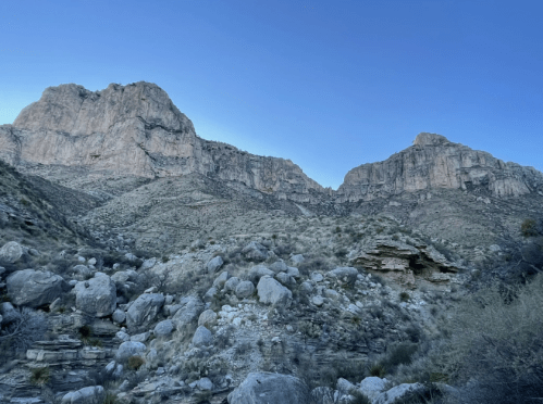 A panoramic view of rugged mountains and rocky terrain under a clear blue sky.