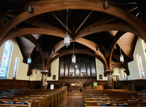 Interior of a church featuring wooden beams, stained glass windows, and an organ at the front.