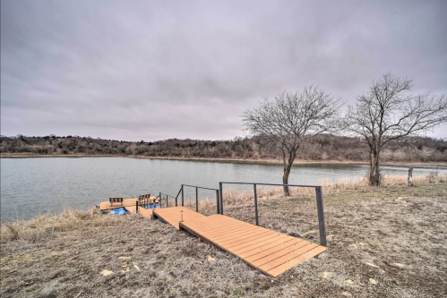 A wooden dock extends into a calm lake, surrounded by bare trees and a cloudy sky.