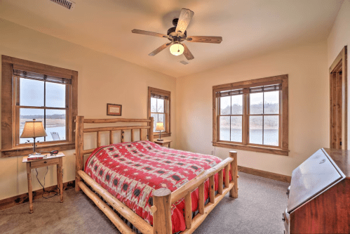 Cozy bedroom with a wooden bed, red patterned blanket, and large windows overlooking a scenic view.