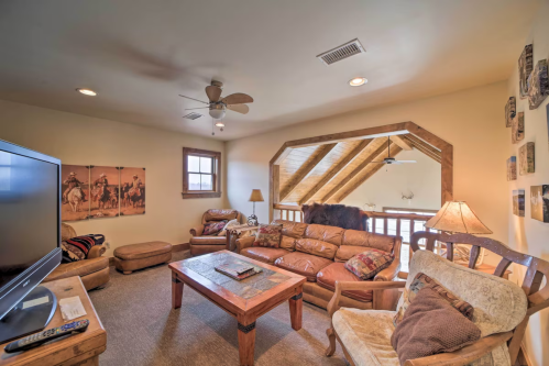 Cozy attic living room with wooden beams, leather furniture, a TV, and decorative wall art.