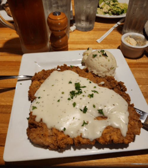 A plate of fried chicken topped with creamy gravy, served with a side of mashed potatoes and garnished with parsley.
