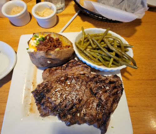 A plate featuring a grilled steak, baked potato topped with cheese and bacon, and a side of green beans.