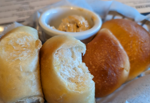 Freshly baked rolls with a side of creamy butter, served in a basket. One roll is partially cut open.