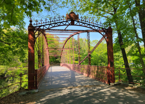 A historic red iron bridge surrounded by lush green trees on a sunny day.