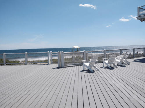 A sunny beachside deck with white chairs facing the ocean and a clear blue sky.
