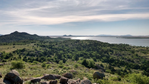 A scenic view of rolling hills and a shimmering lake under a clear blue sky, with distant mountains on the horizon.