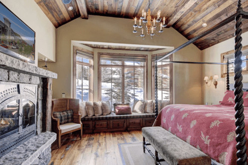 Cozy bedroom with a four-poster bed, stone fireplace, and large windows overlooking a snowy landscape.
