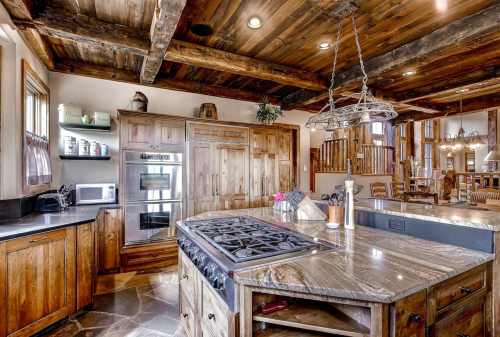 A rustic kitchen featuring wooden cabinets, a large island with a stove, and exposed beam ceilings.