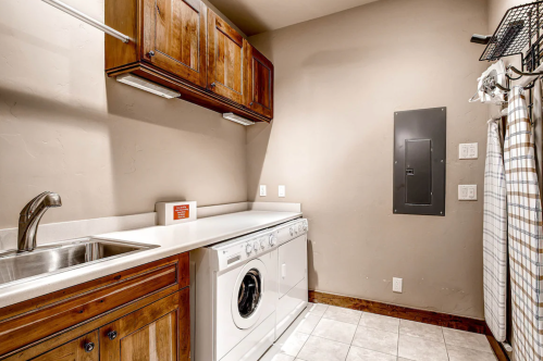 A laundry room featuring a washing machine, sink, wooden cabinets, and neutral-colored walls.