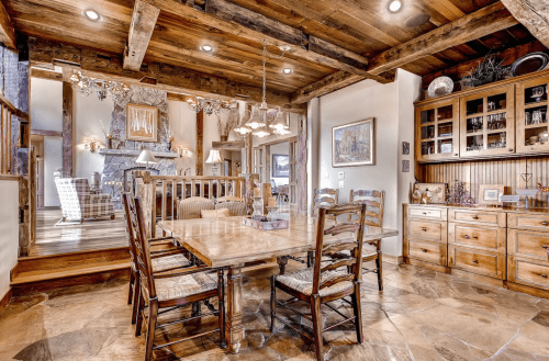 A rustic dining area with a wooden table, chairs, and exposed beams, leading to a cozy living space.