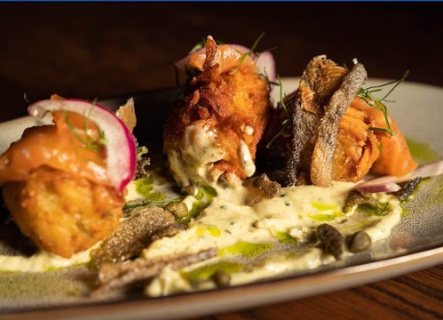 Three gourmet appetizers on a plate, featuring crispy elements, garnished with herbs and drizzled with sauce.