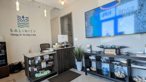 A welcoming reception area of a wellness center, featuring a desk, plants, and a large screen displaying "OPEN."