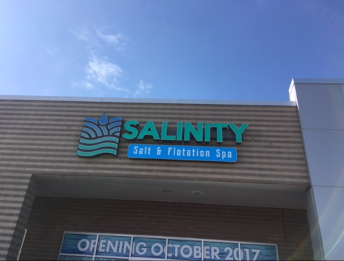 Sign for "SALINITY Salt & Flotation Spa" on a building exterior, with a blue sky in the background.
