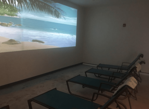 A serene room with lounge chairs and a projection of a beach scene on the wall.