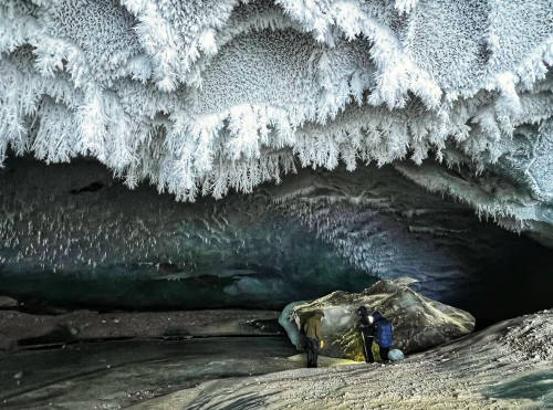 Two explorers in a frozen cave, surrounded by intricate ice formations and a rocky floor.