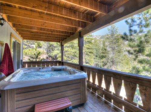 A hot tub on a wooden deck surrounded by trees and mountains, with a red towel hanging nearby.