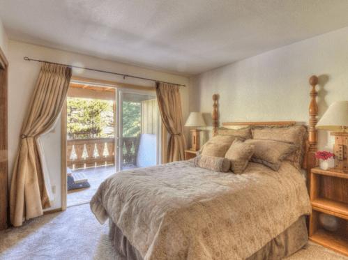 Cozy bedroom with a large bed, decorative pillows, and a balcony door leading to an outdoor view.