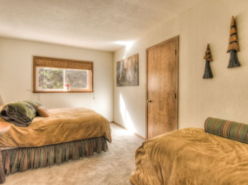 Cozy bedroom with two beds, warm tones, a window, and decorative wall art. Natural light brightens the space.