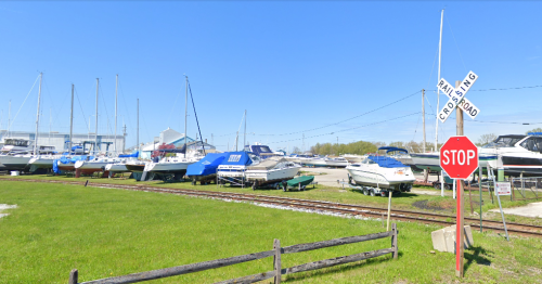 A marina with parked boats, green grass, and a stop sign near a railroad crossing on a clear day.