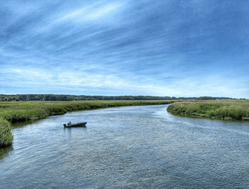 A serene river scene with a small boat and lush green banks under a blue sky with wispy clouds.