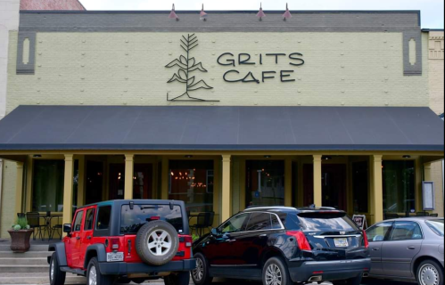 Exterior of Grits Cafe with a yellow brick facade, a black awning, and parked cars in front.