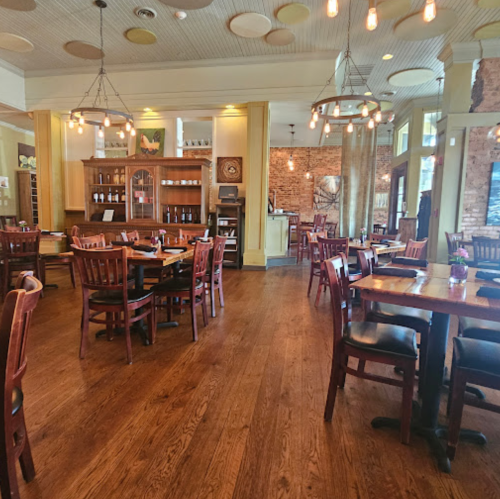 Cozy restaurant interior with wooden tables, chairs, and warm lighting, featuring brick walls and a welcoming atmosphere.
