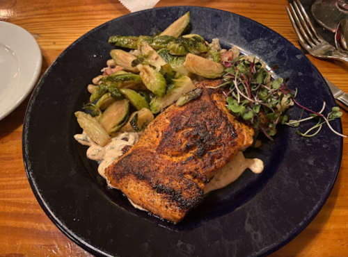 Grilled salmon fillet on a plate with sautéed vegetables and microgreens.