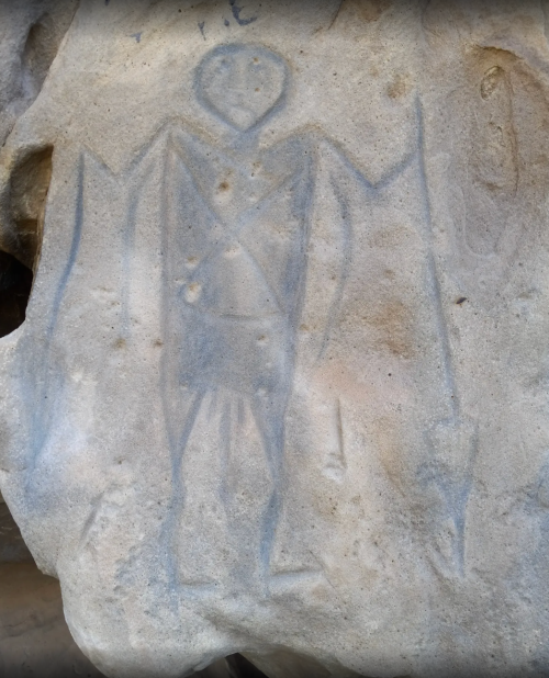Petroglyph of a humanoid figure with outstretched arms, carved into a rocky surface.