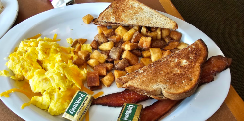 A plate with scrambled eggs, crispy bacon, golden hash browns, and two slices of toasted bread with butter.