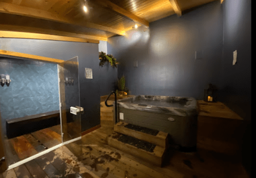 A cozy spa room featuring a hot tub, wooden accents, and soft lighting, creating a relaxing atmosphere.