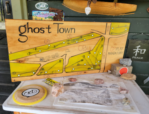 A wooden sign labeled "Ghost Town" with a map layout, surrounded by rocks and a frisbee on a table.