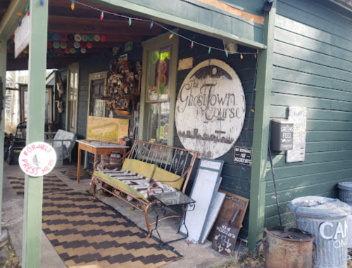 A quaint storefront with a sign reading "Ghost Town Course," featuring vintage decor and a welcoming porch.