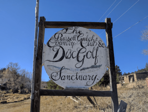 Sign for "The Russell Gulch Country Club & Disc Golf Sanctuary" against a clear blue sky.