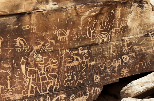 Ancient petroglyphs etched into a rocky surface, depicting various symbols and figures in earthy tones.