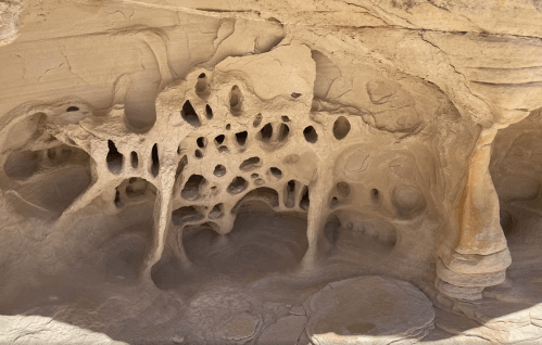 Intricate rock formations with holes and cavities, showcasing natural erosion patterns in a sandy landscape.