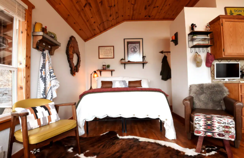 Cozy bedroom with a wooden ceiling, a bed, two chairs, and rustic decor, creating a warm and inviting atmosphere.