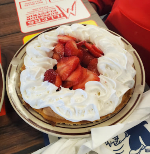 A dessert featuring a fluffy pancake topped with whipped cream and fresh strawberries on a plate.