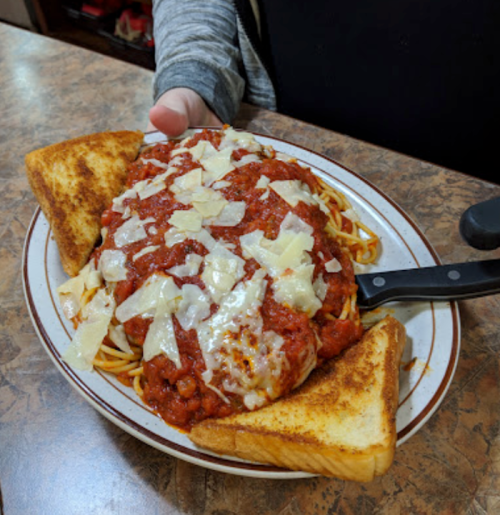 A plate of spaghetti topped with marinara sauce and cheese, served with two slices of toasted bread.