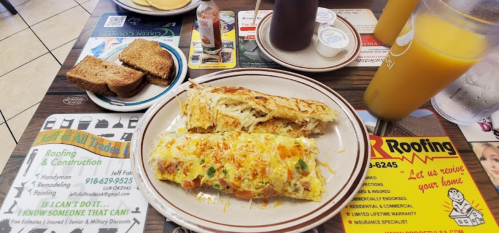 A plate with an omelet, hash browns, toast, and drinks on a table with various menus and advertisements.